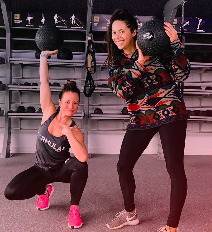 two women posing for the camera with strength training equipment